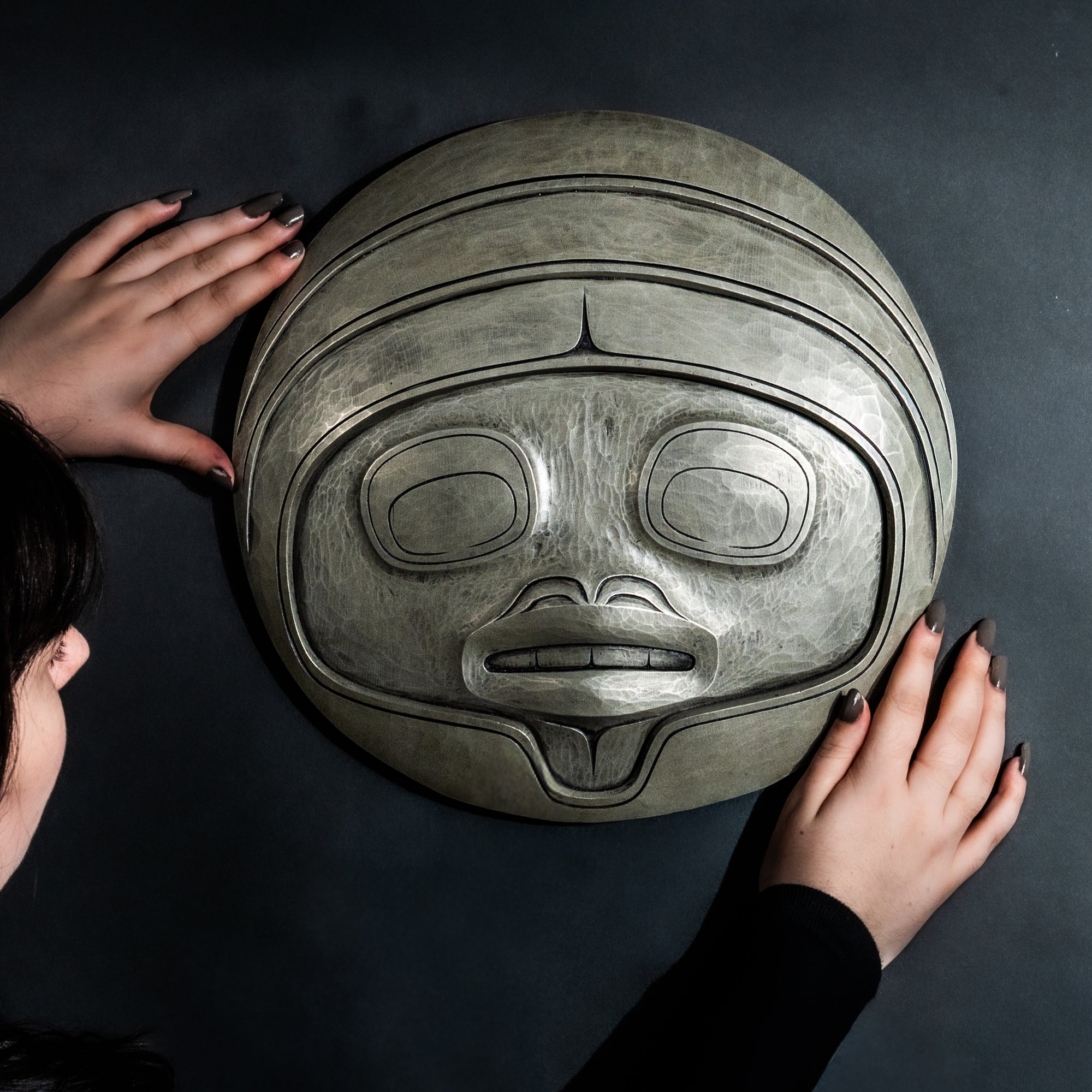 Person holding Fungus man mask casting with intricate carvings by Haida artist Cori Savard against a dark background