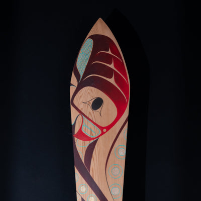 Close up of Wooden paddle with artistic red and blue formline octopus design on a black background