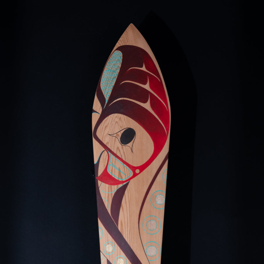 Close up of Wooden paddle with artistic red and blue formline octopus design on a black background