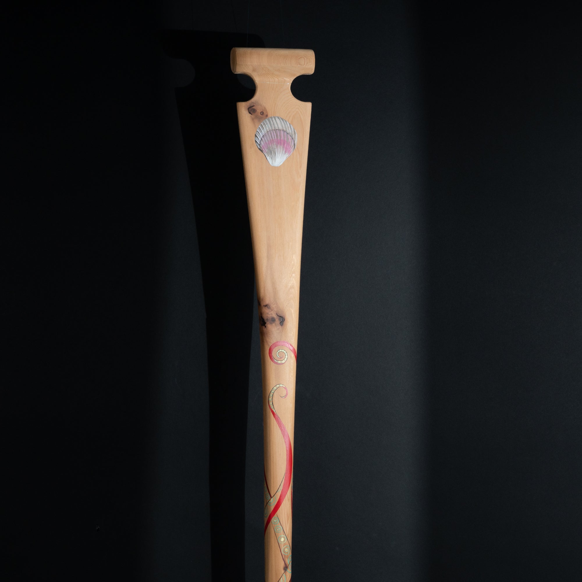 Wooden paddle with shell and red tentacles design on a black background