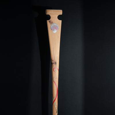 Wooden paddle with shell and red tentacles design on a black background
