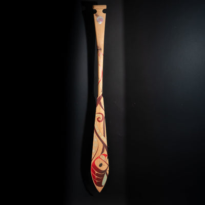 Wooden paddle with artistic red and blue formline octopus design reaching for a clam shell by Haida artist Danielle Louis Allard on a black background