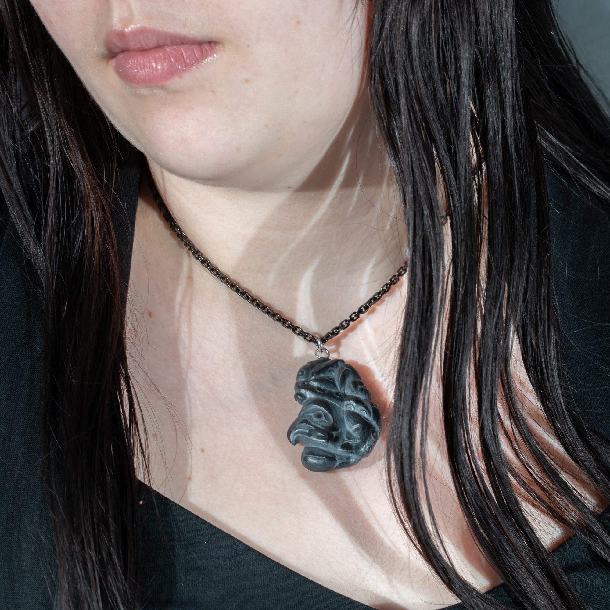 Close up of tentacles wrapping around both sides of Black Argillite Octopus pendant necklace with intricate Haida Carvings on a white background made by Local Haida Gwaii Artist Melanie Russ
