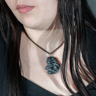 Close up of tentacles wrapping around both sides of Black Argillite Octopus pendant necklace with intricate Haida Carvings on a white background made by Local Haida Gwaii Artist Melanie Russ