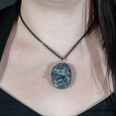 Black Argillite Sea Bear pendant necklace with intricate Haida Carvings on a white background made by Local Haida Gwaii Artist Melanie Russ worn by a person