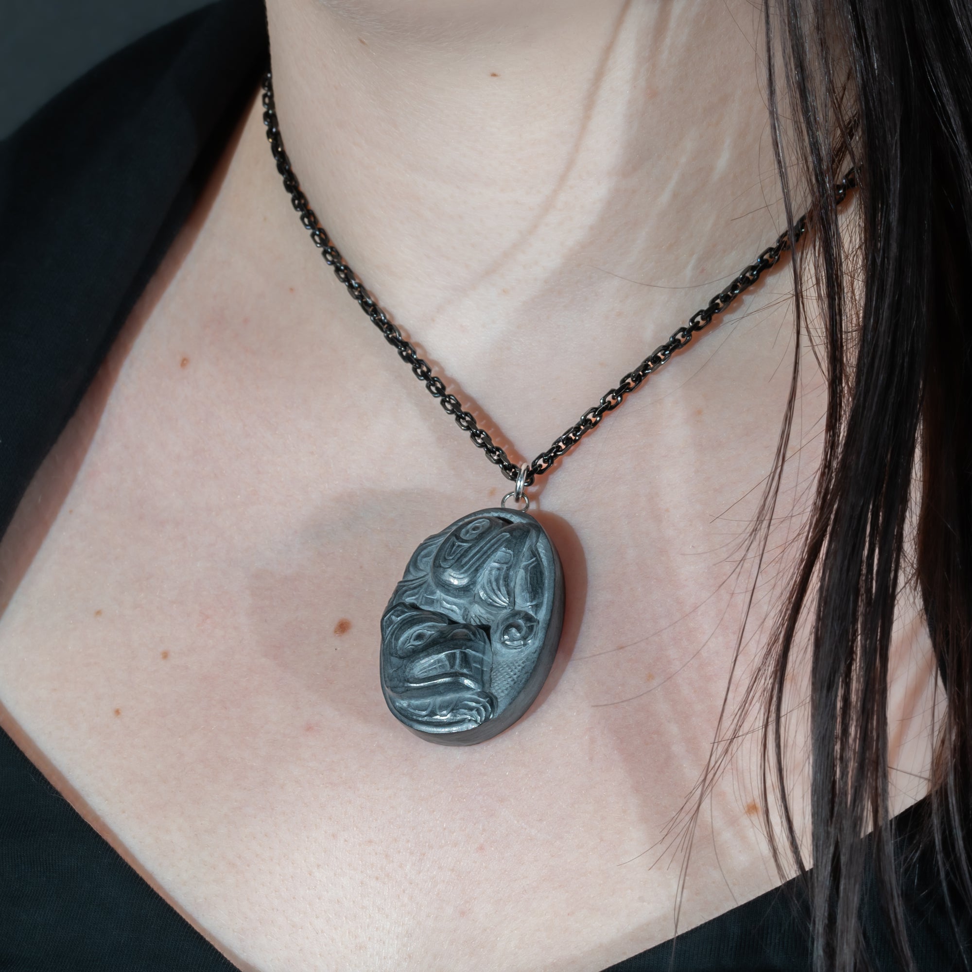 Black Argillite Sea Bear pendant necklace with intricate Haida Carvings on a white background made by Local Haida Gwaii Artist Melanie Russ worn by a person