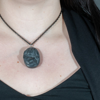Black Argillite Sea Bear pendant necklace with intricate Haida Carvings on a white background made by Local Haida Gwaii Artist Melanie Russ worn by a person against a black background