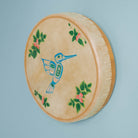 Drum with beige hide and light wood with a blue bird design and green floral leaves on a light blue backgroung