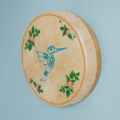 Drum with beige hide and light wood with a blue bird design and green floral leaves on a light blue backgroung