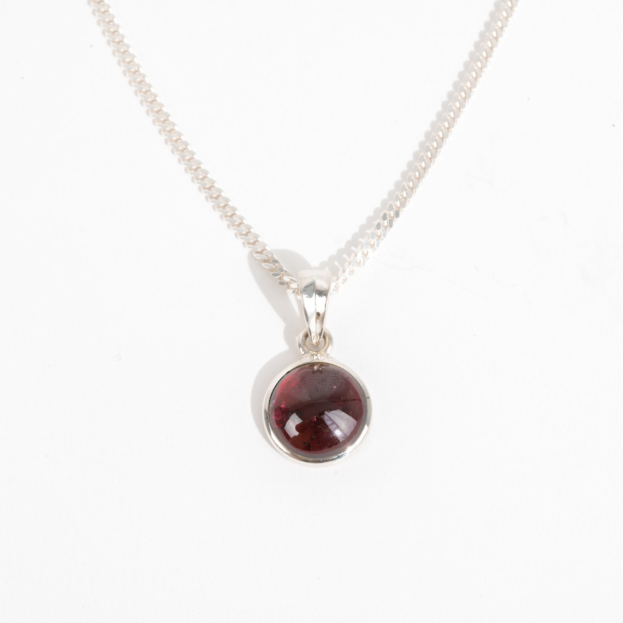 Silver necklace with a round red garnet gemstone pendant for January's birthstone on a white background