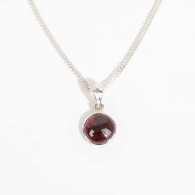 Silver necklace with a round red garnet gemstone pendant for January's birthstone on a white background