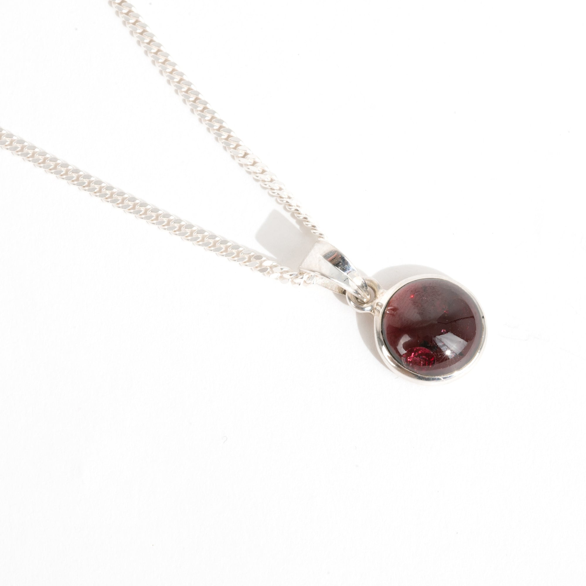 A round red garnet necklace that angles to the right side hung on a sterling silver curb chain