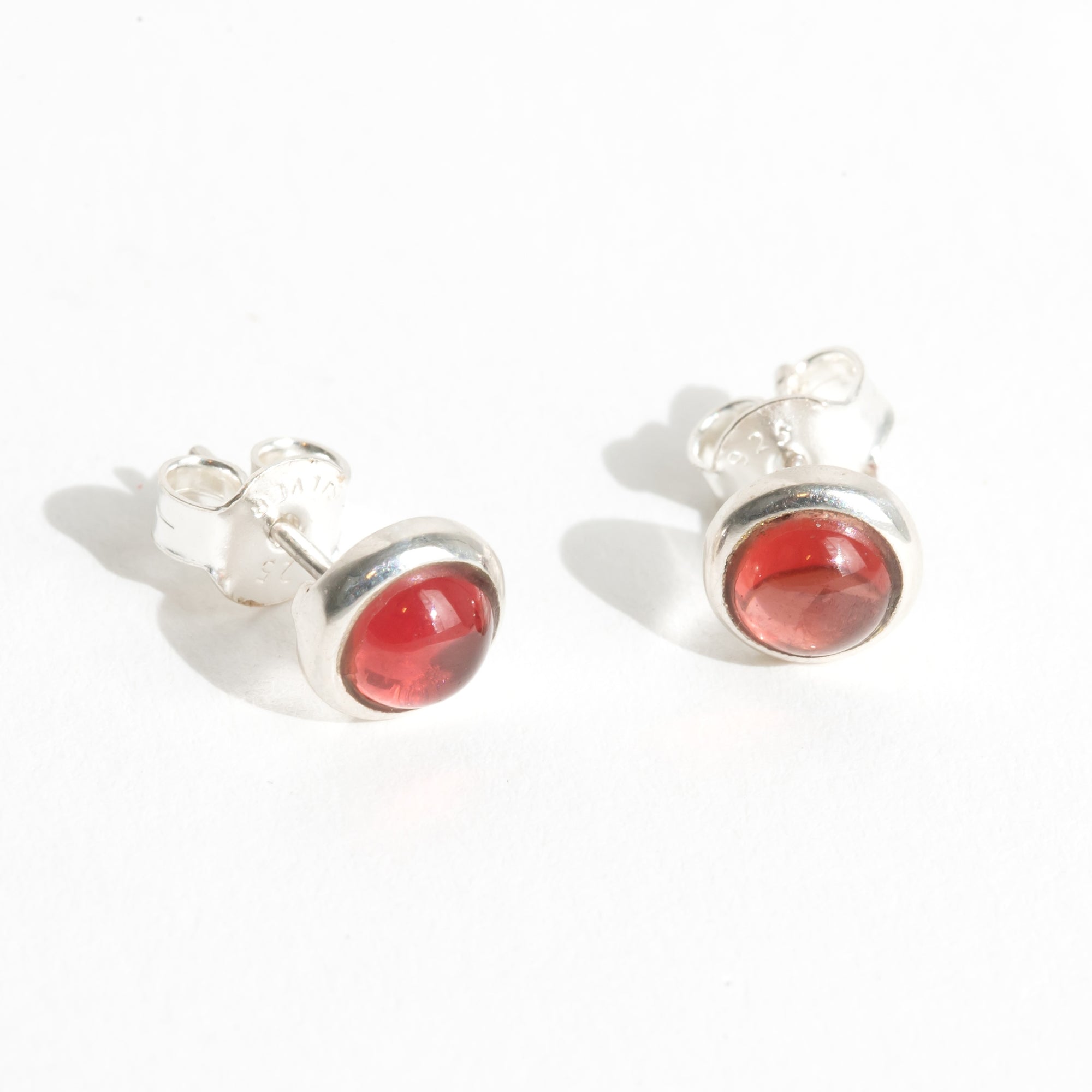 Silver earrings with red garnet gemstones for Januarys birthstone on a white background