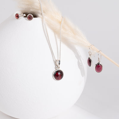 Jewelry set with red garnet gemstones by a white vase with a strand of yellow dried grass.