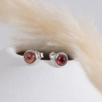 Silver earrings with red garnet gemstones on a white surface with a piece of straw to the right.