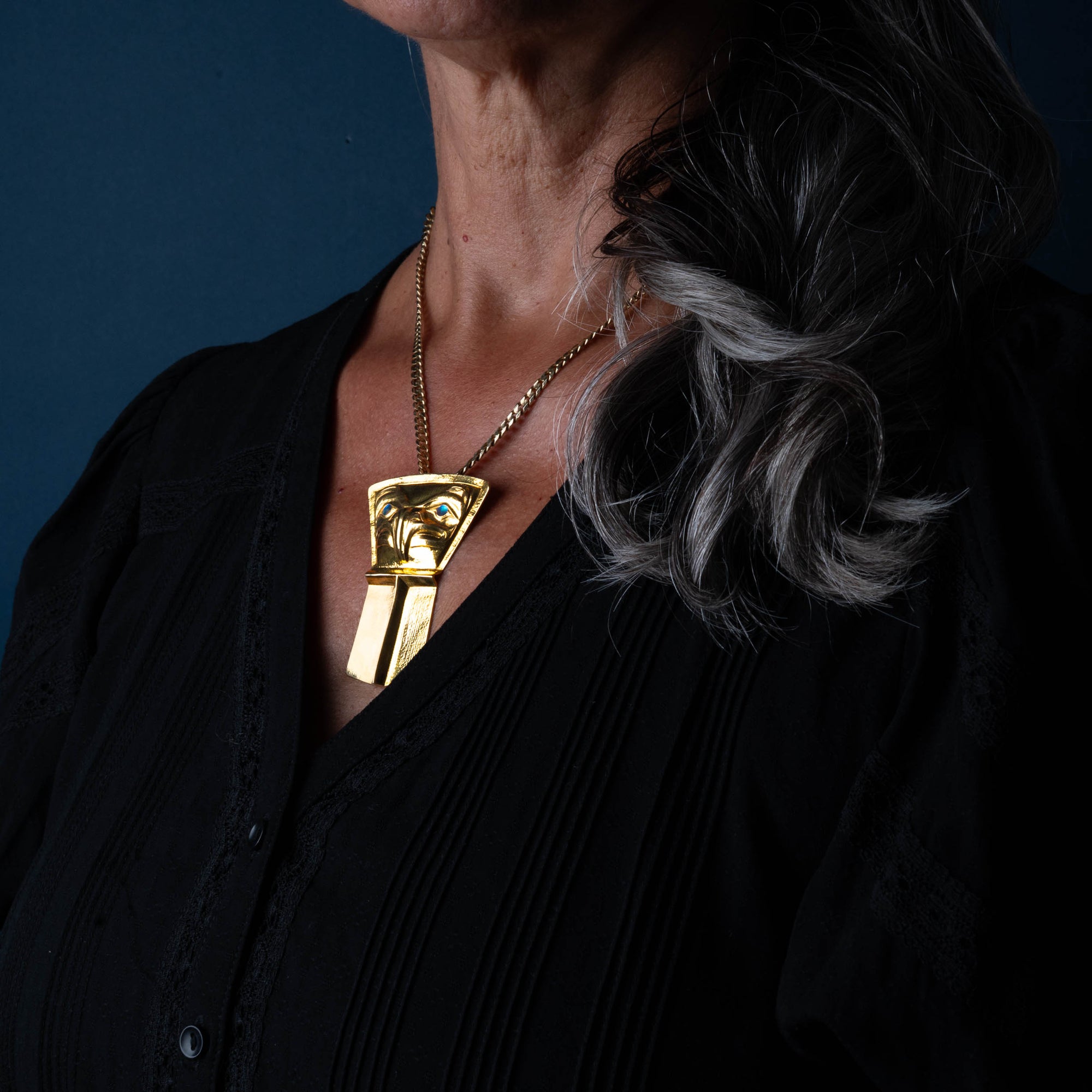 A woman wearing a 22k gold Jesse Brillon pendant with grey hair on her left shoulder