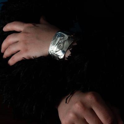 Close-up of hands with a Sterling Silver cuff bracelet with intricate Eagle and Salmon Repoussé design