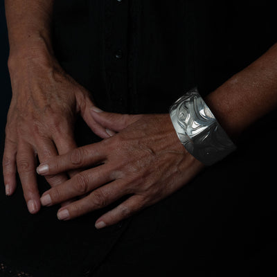 Close-up of hands with a Sterling Silver cuff bracelet with intricate Eagle and Salmon Repoussé design on a black background