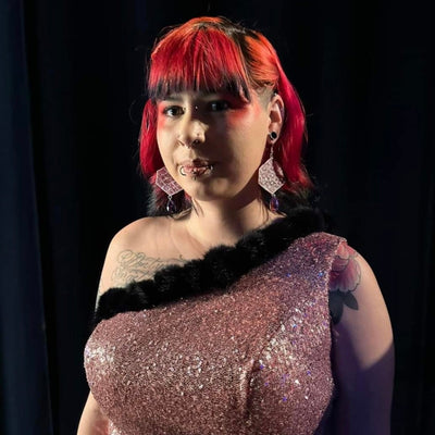 Model with red hair wearing pink earrings and a sparkly dress against a black background.