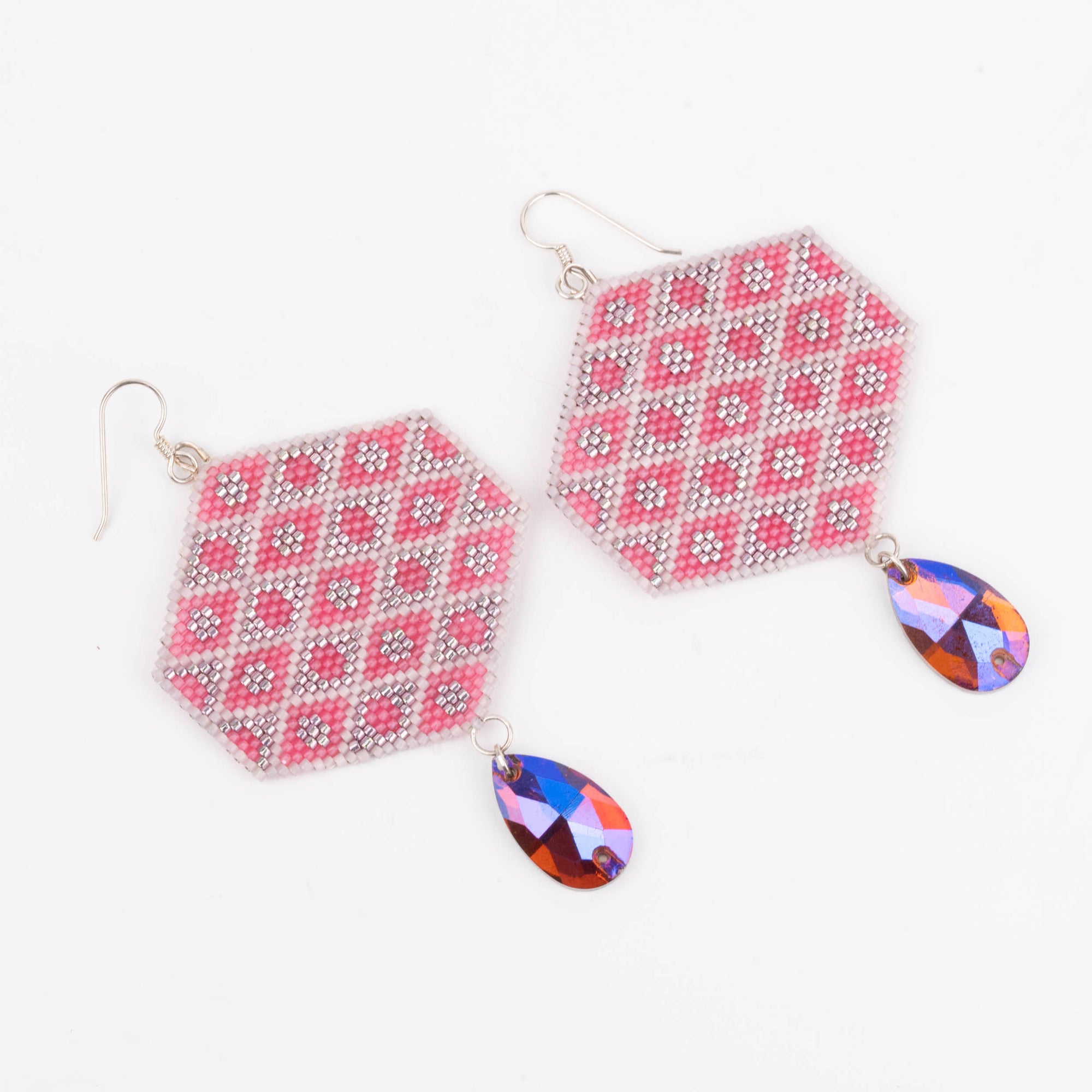 Hexagonal patterned earrings with colorful teardrop charms on a white background photographed on an angle.