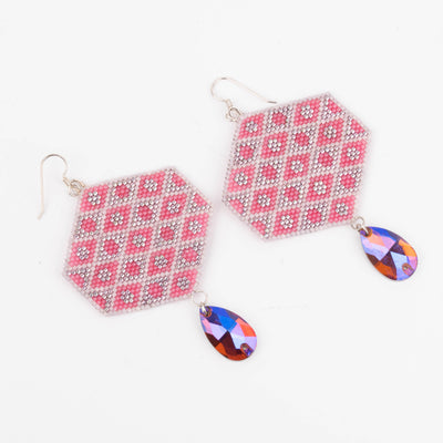 Hexagonal patterned earrings with colorful teardrop charms on a white background photographed on an angle.