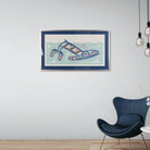 Framed artwork of Kun (whale) Fine art print, showcasing a whale swimming through the ocean in Haida Formline. Set in an Interior design on a wall above a modern blue chair.