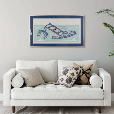 White sofa with decorative pillows in a room with a framed artwork of Kun (whale) Fine art print, showcasing a whale swimming through the ocean in Haida Formline on the wall.