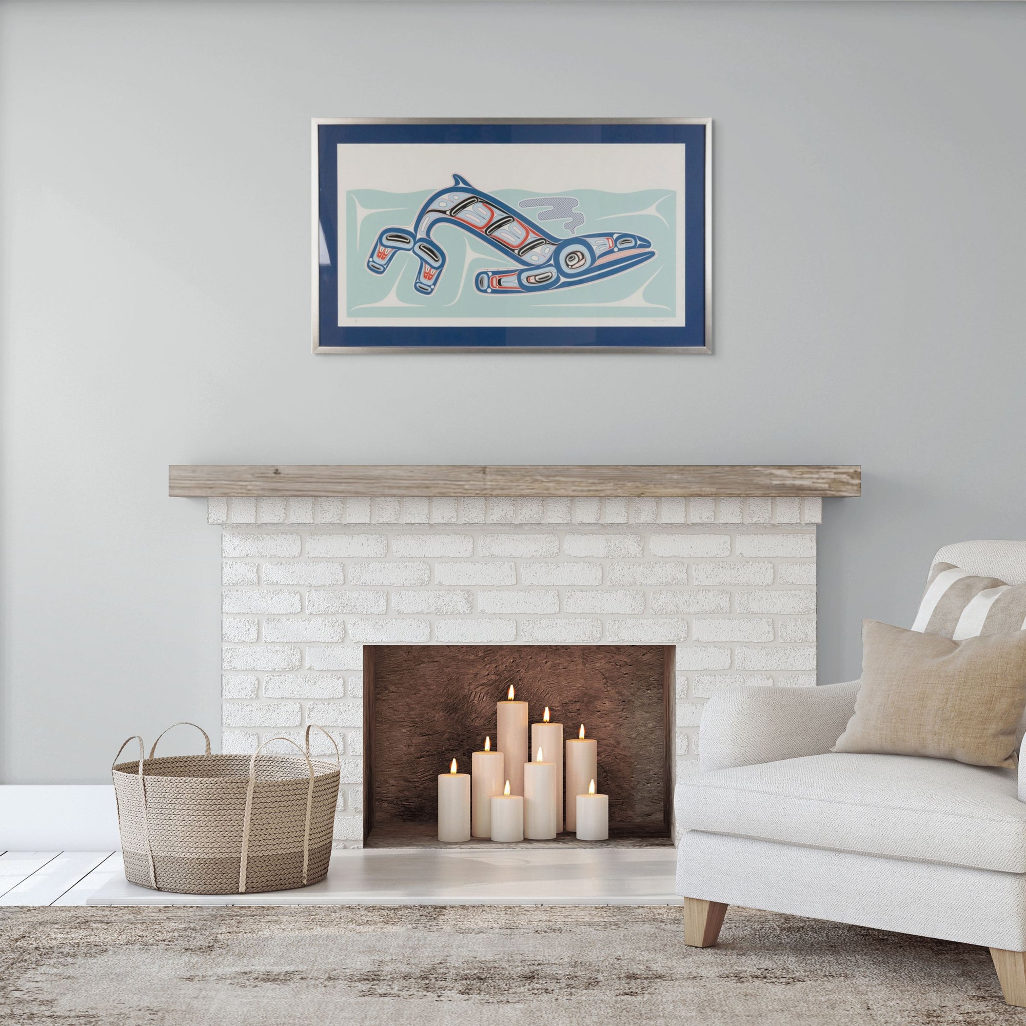 Living room with a white brick fireplace, candles, a basket, and a framed artwork above of Kun (whale) Fine art print, showcasing a whale swimming through the ocean in Haida Formline. Set in an Interior design