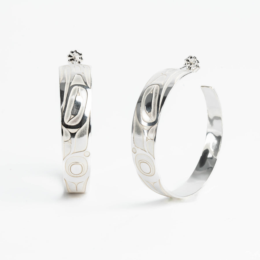 Pair of silver hoop earrings with intricate formline Ts'ymsen thunderbird designs on a white background
