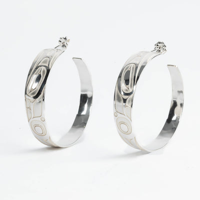 Pair of silver hoop earrings with intricate formline Ts'ymsen thunderbird designs on a white background
