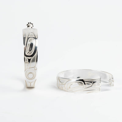 Pair of silver hoop earrings with intricate formline Ts'ymsen thunderbird designs on a white background