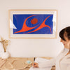 Woman sitting at a desk with a colorful red and blue abstract painting of two dancing by Robert Davidson on the wall