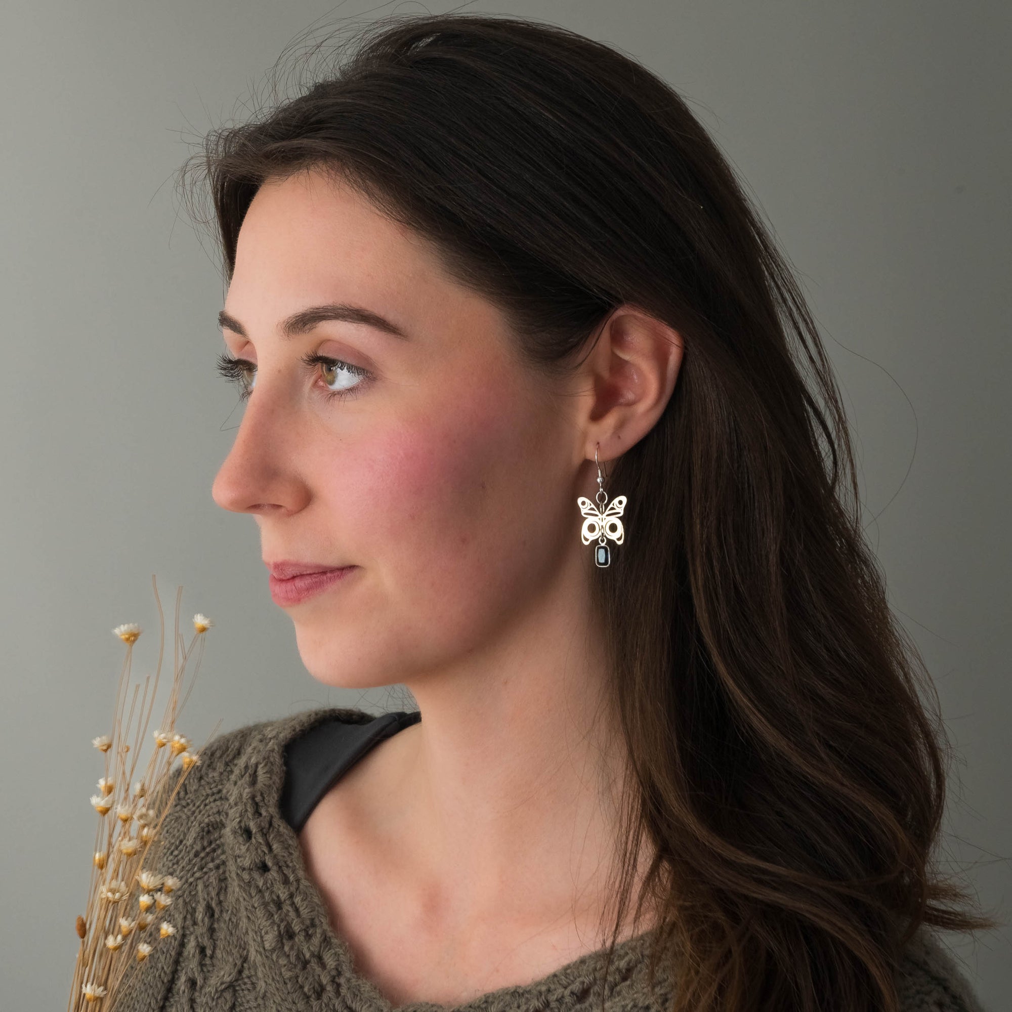 Woman wearing butterfly earrings against a neutral background