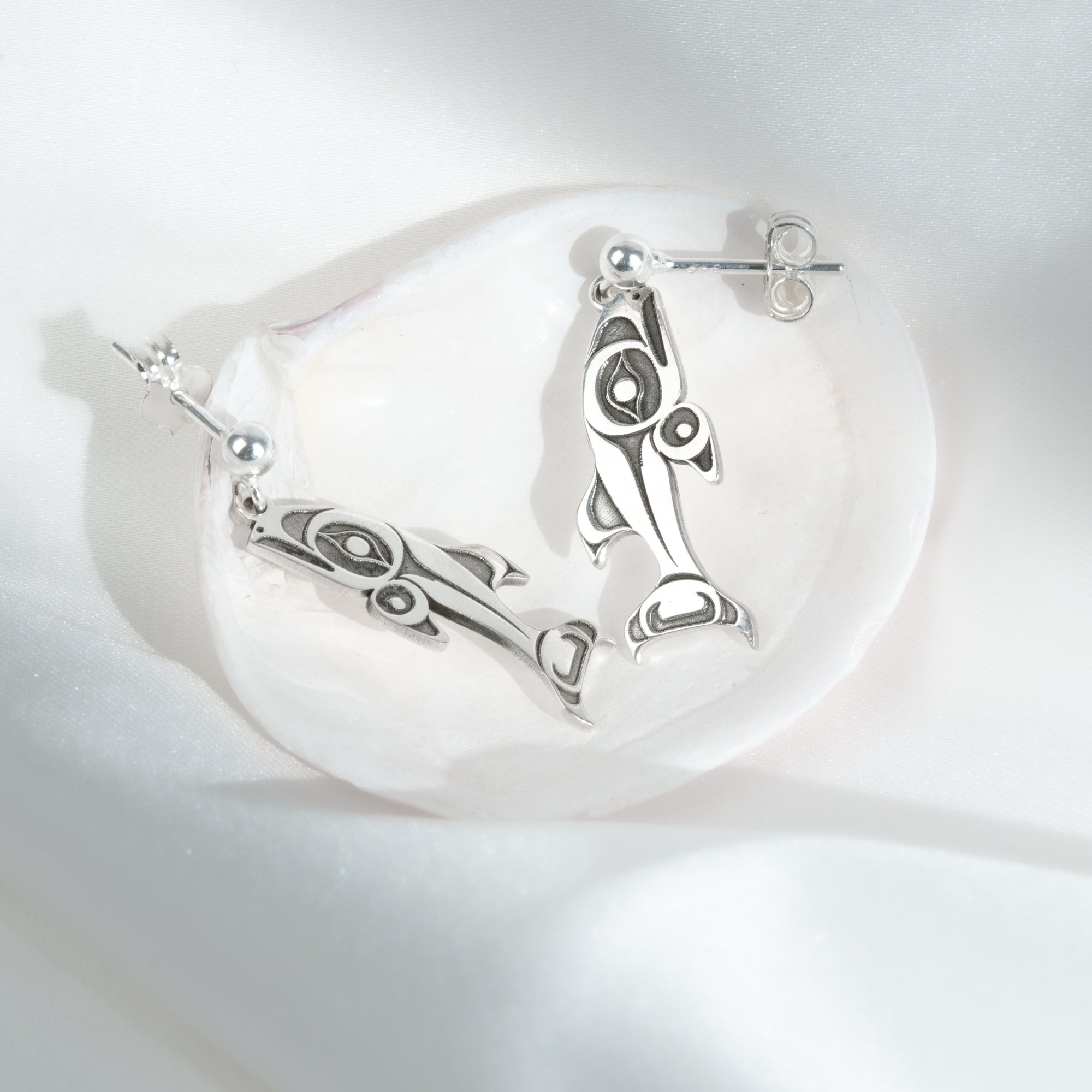 Sterling Silver Salmon earrings on a clam shell on a white silk backgroung by Native artist Morgan Asoyuf