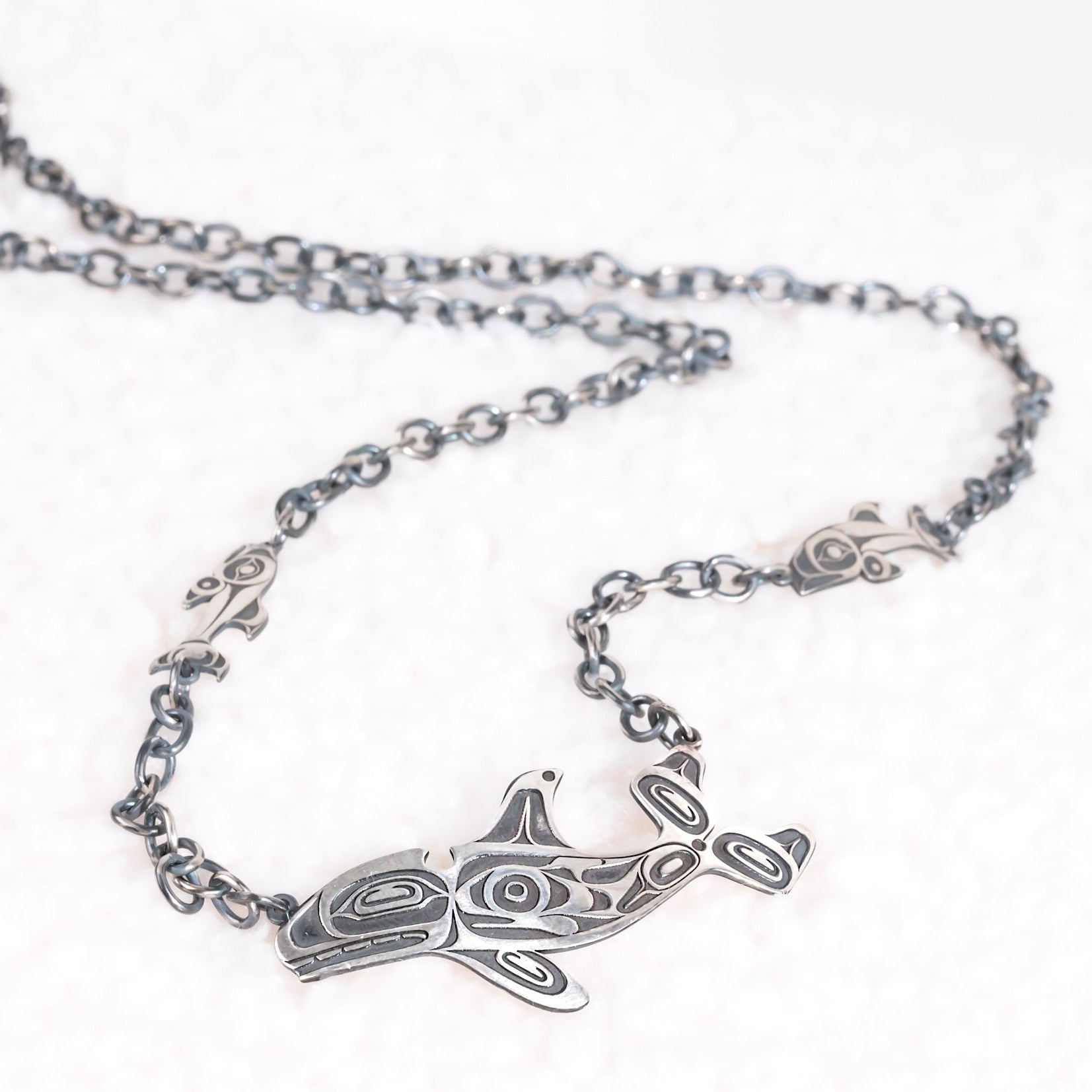 Silver necklace with a killer whale pendant  and salmon on a white background by Native Canadian artist morgan Asoyuf