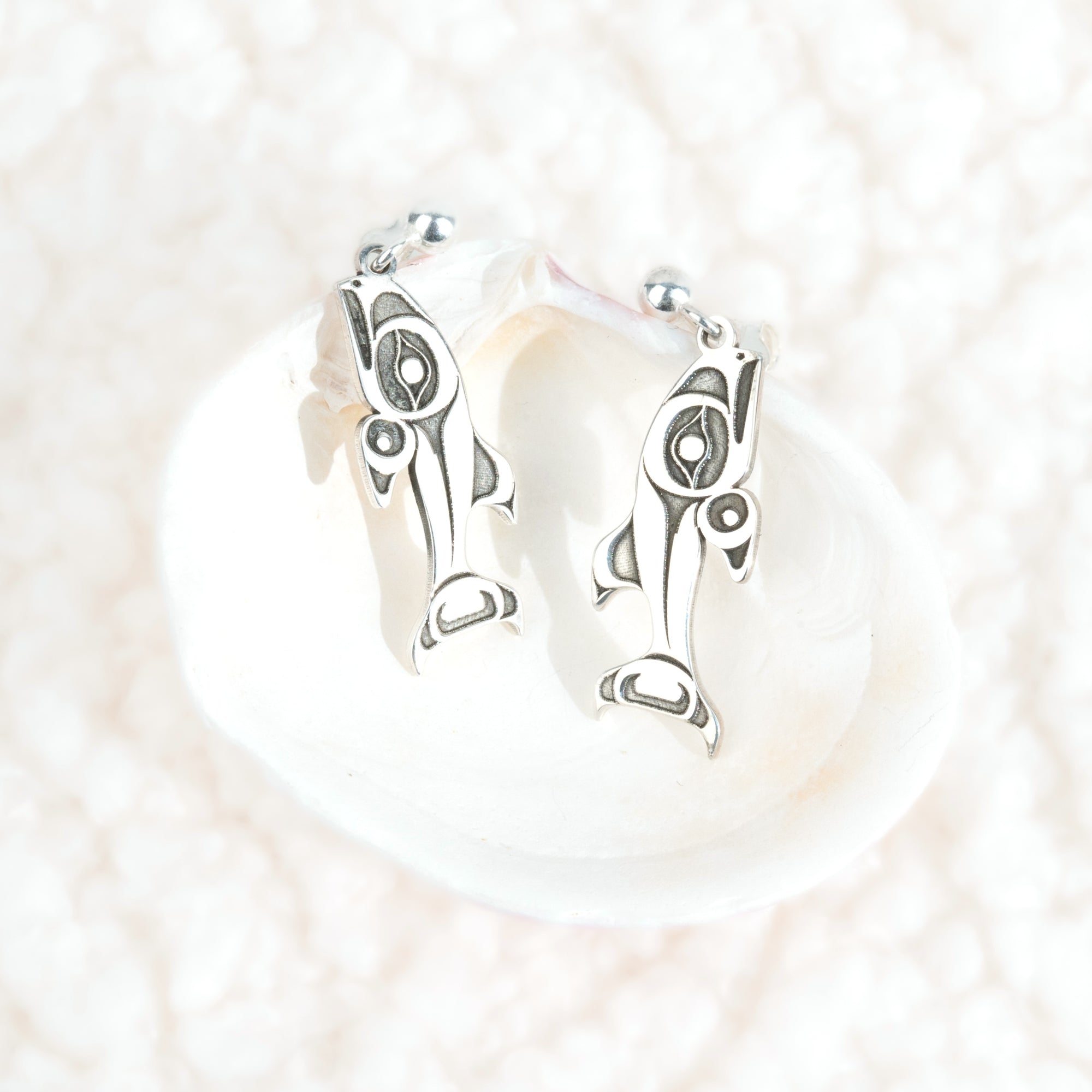 Sterling Silver Salmon earrings on a clam shell on a white cloud like background by Native artist Morgan Asoyuf
