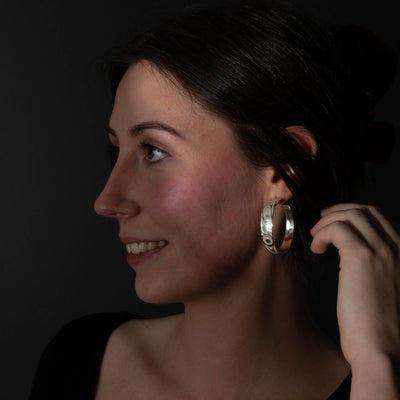 Pair of silver hoop earrings with intricate formline Ts'ymsen thunderbird designs worn by model