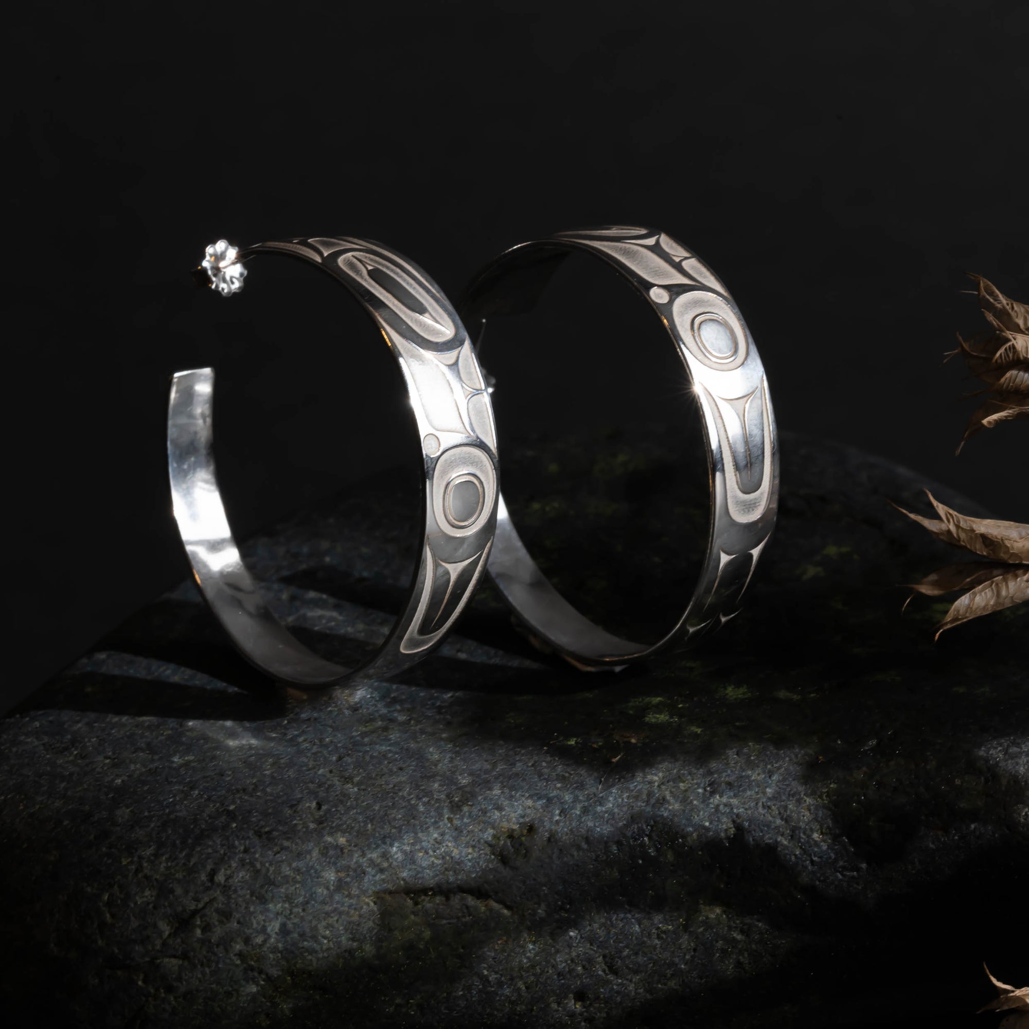 Pair of silver hoop earrings with intricate formline Ts'ymsen thunderbird designs in a room set up close up