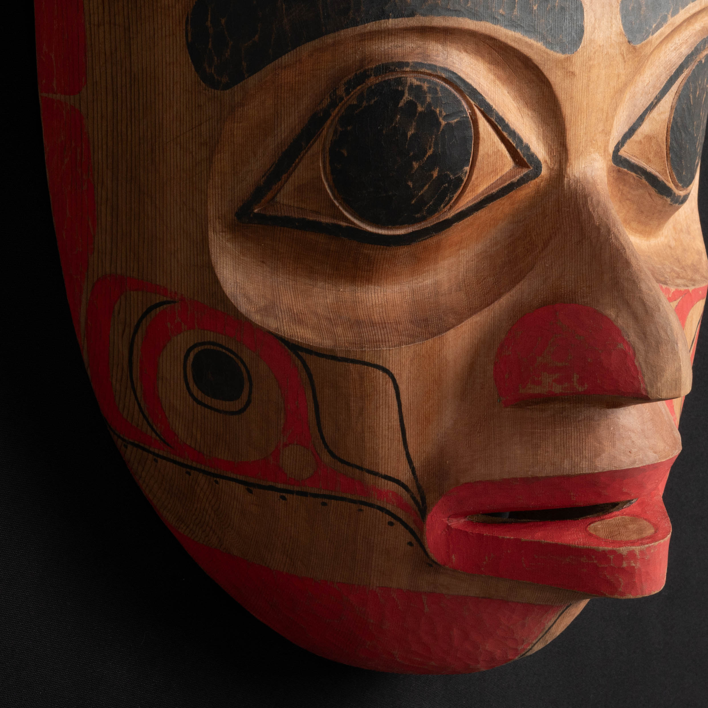 Close up oOrnate Cedar Mouse Woman mask with teal top and black and red face done by Haida artist Corey Bulpitt on a black background 