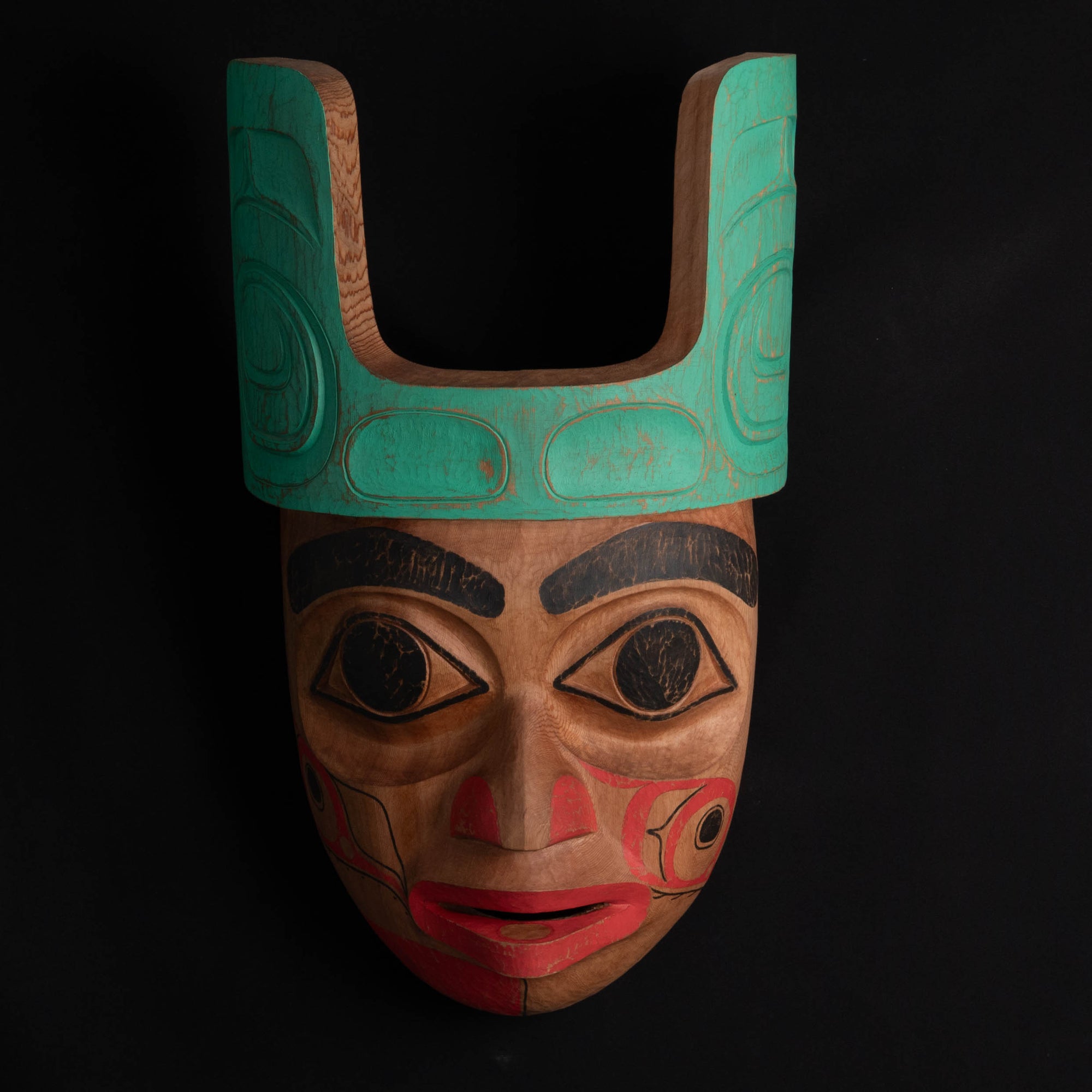 Ornate Cedar Mouse Woman mask with teal top and black and red face done by Haida artist Corey Bulpitt on a black background