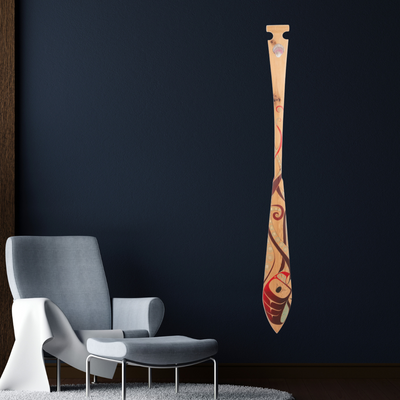 Decorative wall decal of a wooden paddle with tribal design on a dark wall next to a modern chair.