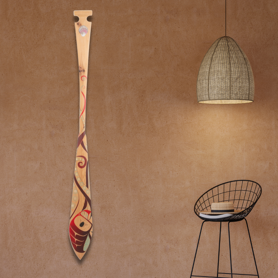 Decorative paddle with artistic design on a brown wall with a black wire chair and hanging light.