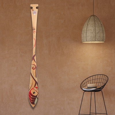 Decorative paddle with artistic design on a brown wall with a black wire chair and hanging light.