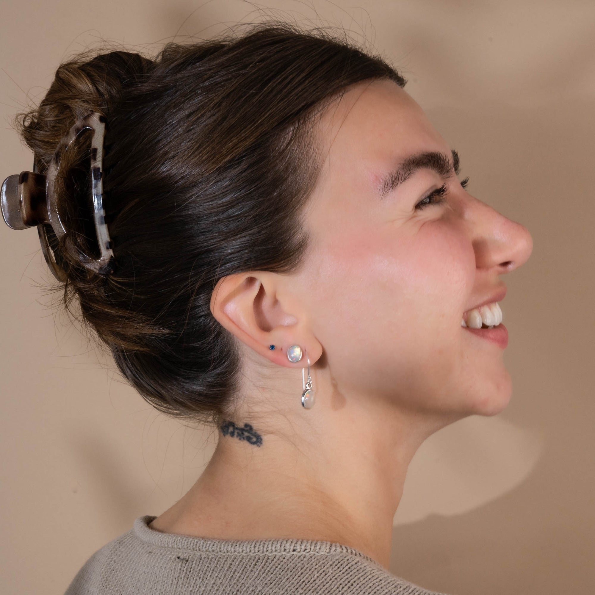 Woman with a bun and Pair of silver earrings with opal stones against a beige background