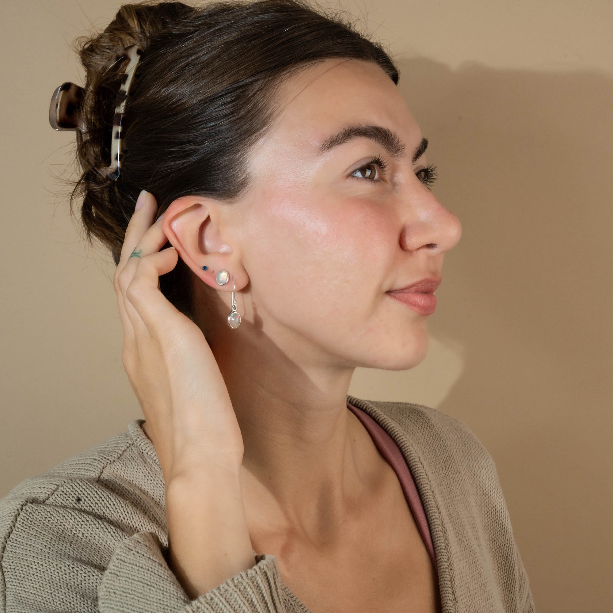Woman adjusting an earring against a neutral background wearing a Pair of silver earrings with opal stones