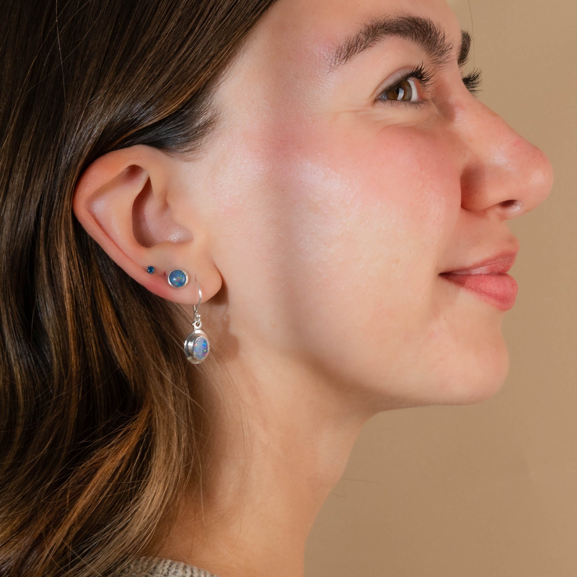 Close-up of a woman wearing silver earrings with blue gemstones on a beige background