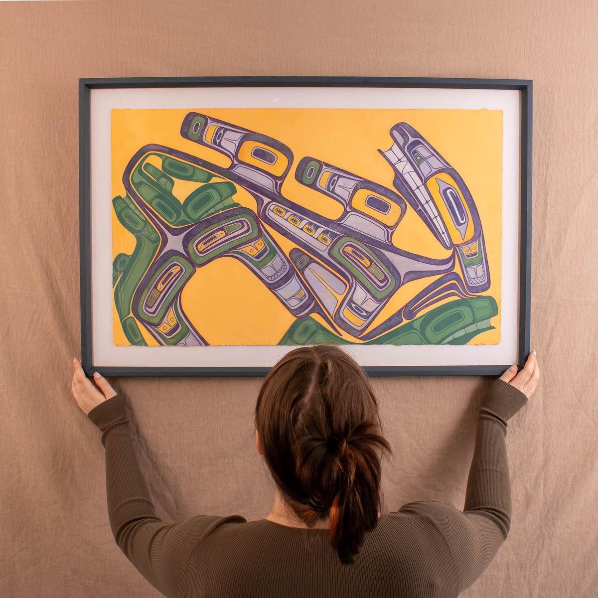 Person holding a framed abstract artwork with geometric shapes on a beige wall