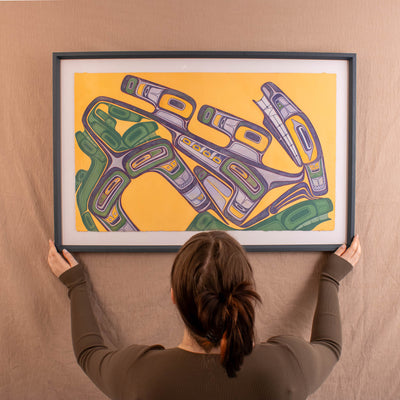 Person holding a framed abstract artwork with geometric shapes on a beige wall