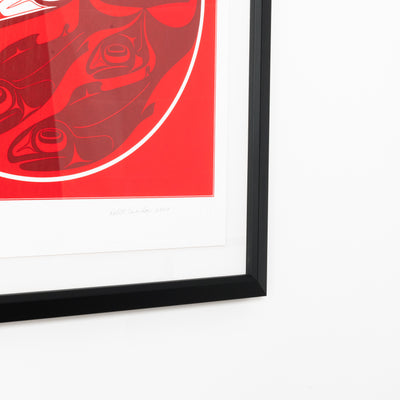 Framed artwork with a red background and black frame on a white surface featuring iconic haida artist Robert Davidsons Formline design