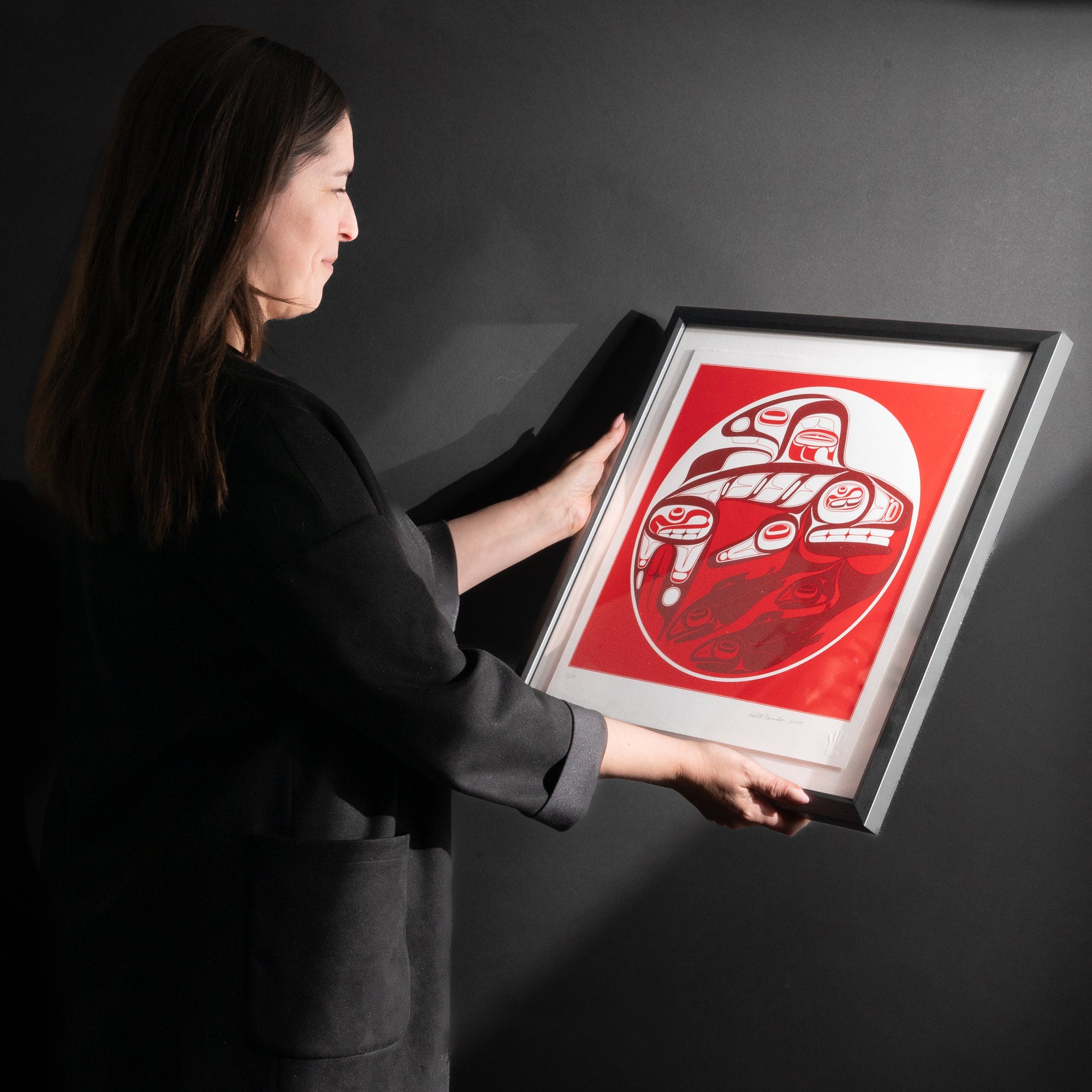 Model admiring Framed Killer whale and Salmon fine Art print by renowned Haida Artist, Robert Davidson on a black background